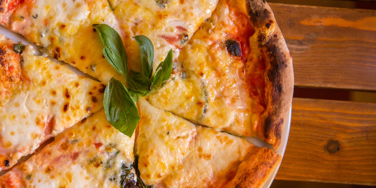A cheese pizza garnished with basil leaves sits on a wood table A cheese pizza garnished with basil leaves sits on a wood table