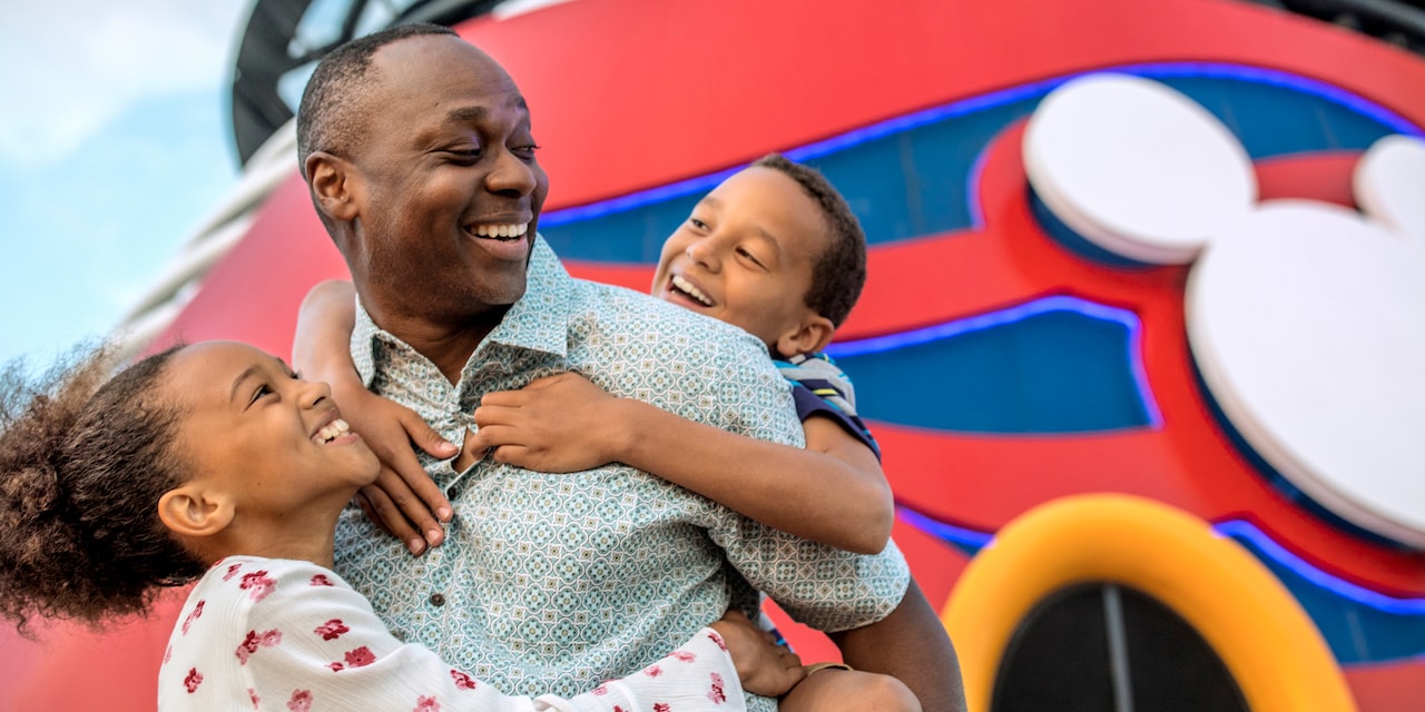 A young boy and girl hug their smiling father near the Forward Funnel of the Disney Magic cruise ship A young boy and girl hug their smiling father near the Forward Funnel of the Disney Magic cruise ship