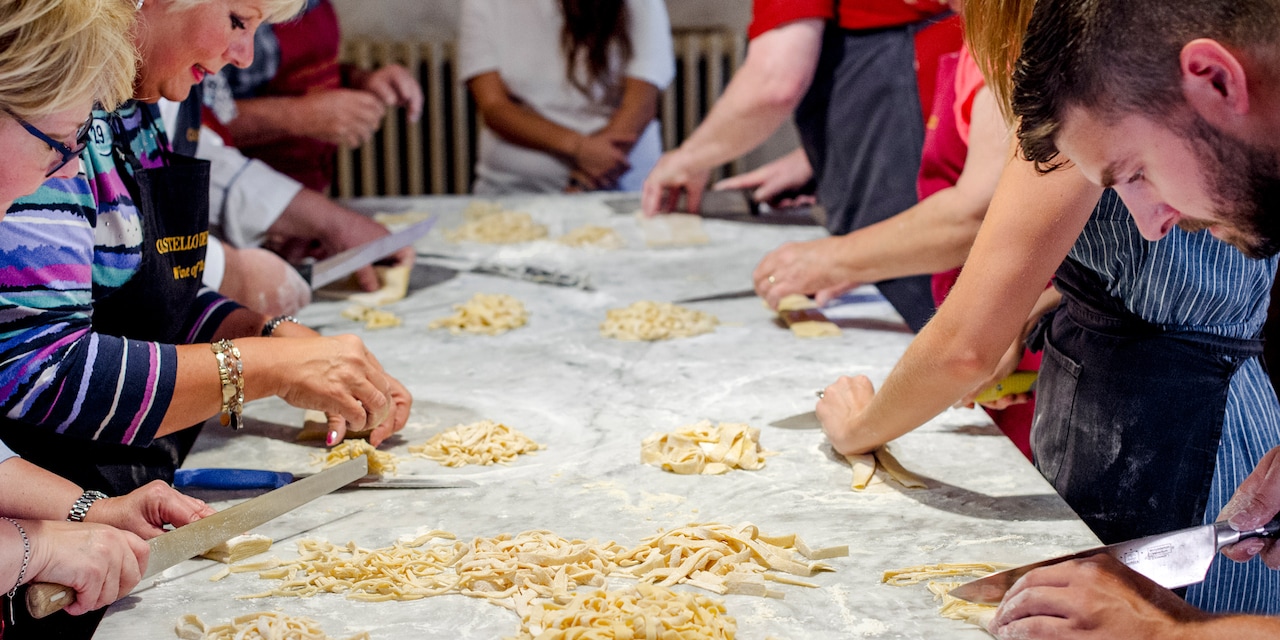A group in a cooking class utilize kitchen utensils and ingredients on a table as an instructor watches from the head of the table A group in a cooking class utilize kitchen utensils and ingredients on a table as an instructor watches from the head of the table