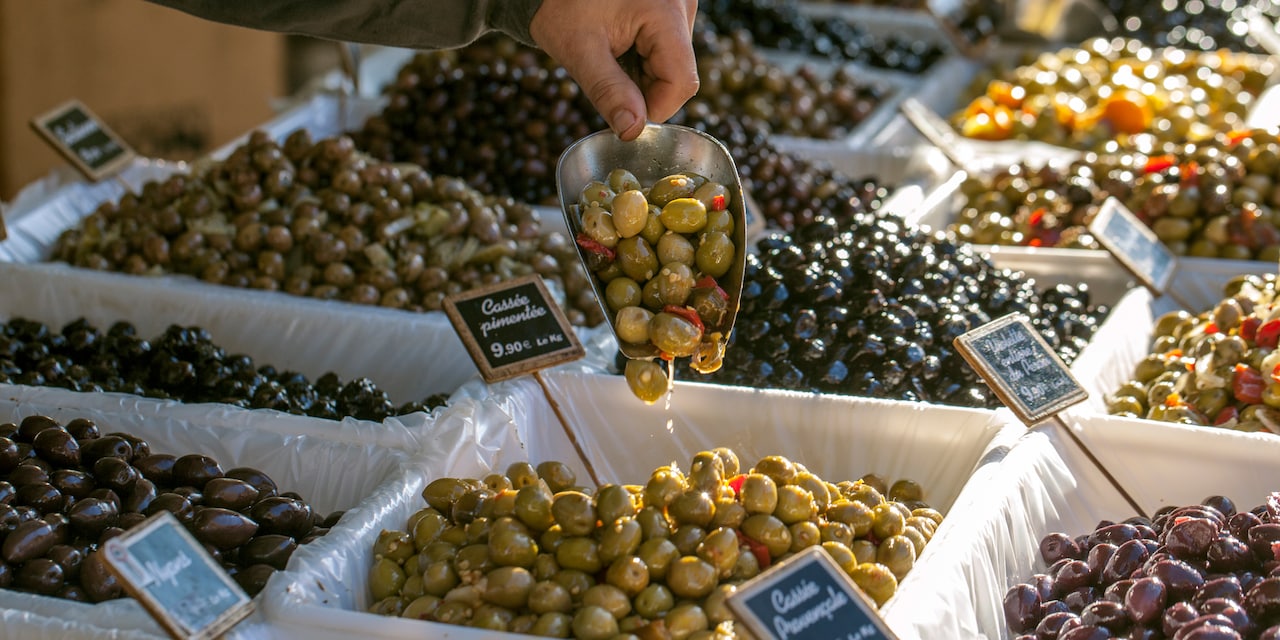 A hand holds a scoop full of olives taken from one of many olive bins at a market A hand holds a scoop full of olives taken from one of many olive bins at a market