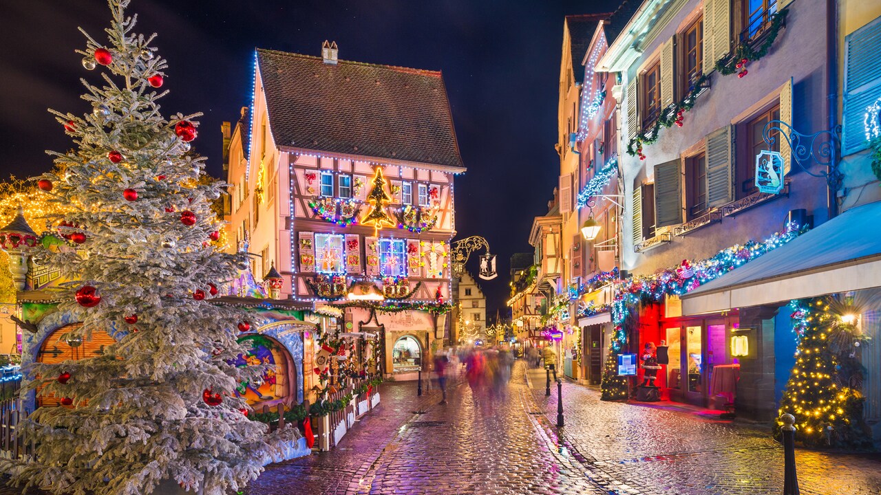 A cobblestone street in Strasbourg, France lined with shops decorated for Christmas lit up at night