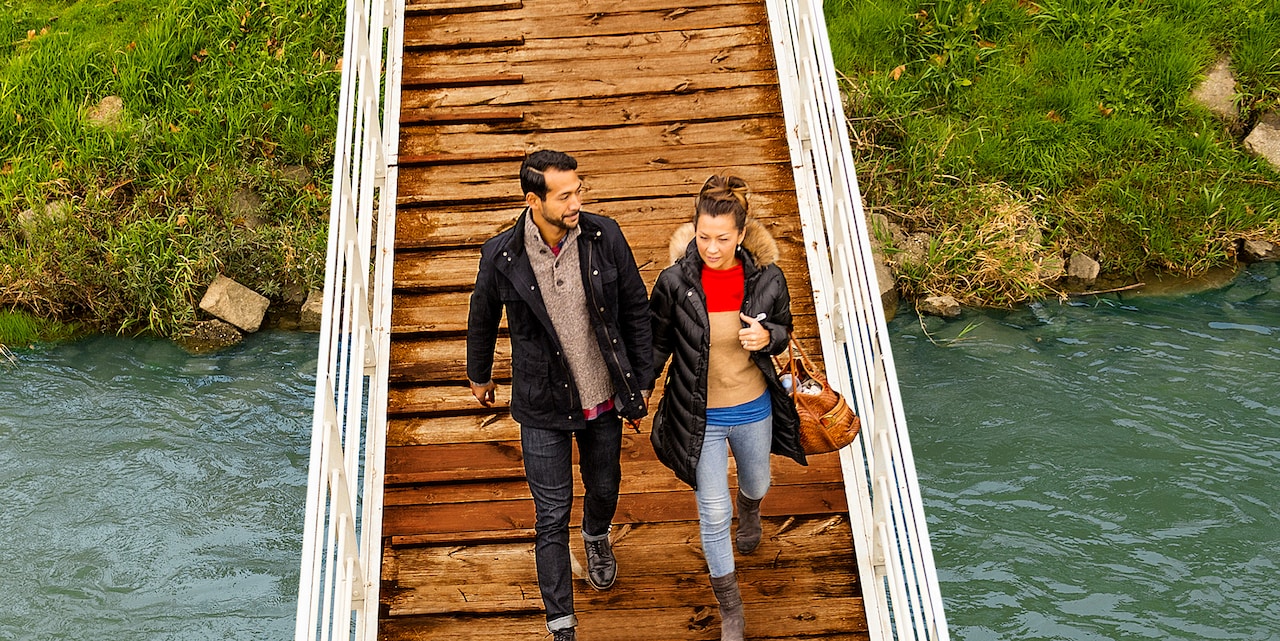 A couple walks across a wooden gangway over the river