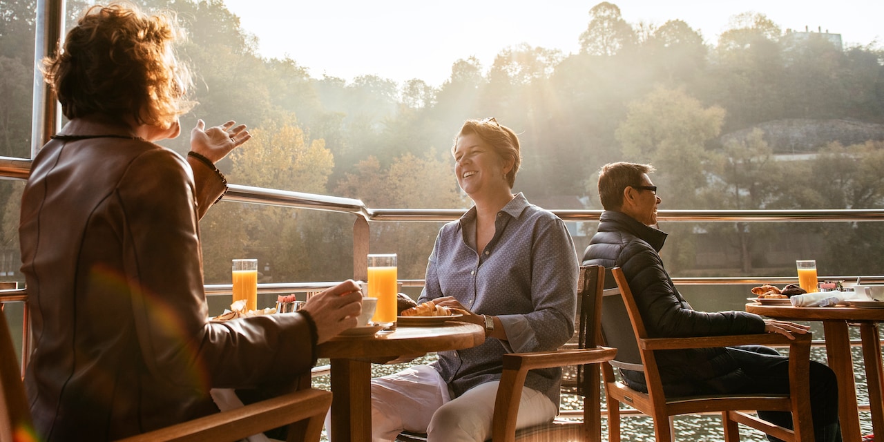 Several Adventurers sit at tables on an outdoor deck aboard a river cruise ship Several Adventurers sit at tables on an outdoor deck aboard a river cruise ship