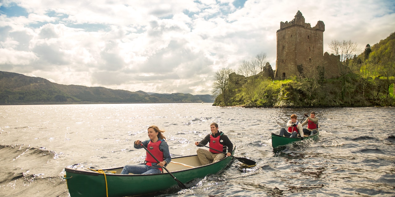 People on 2 rowboats paddling away from a castle on a blustery day People on 2 rowboats paddling away from a castle on a blustery day