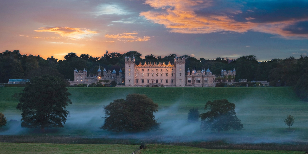 The majestic Floors Castle sits perched atop a grassy plateau as a hot air balloon hovers nearby