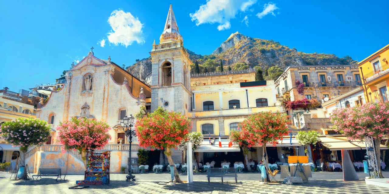 San Guiseppe church and tree-line plaza with restaurant tables set up under an awning in Taormina