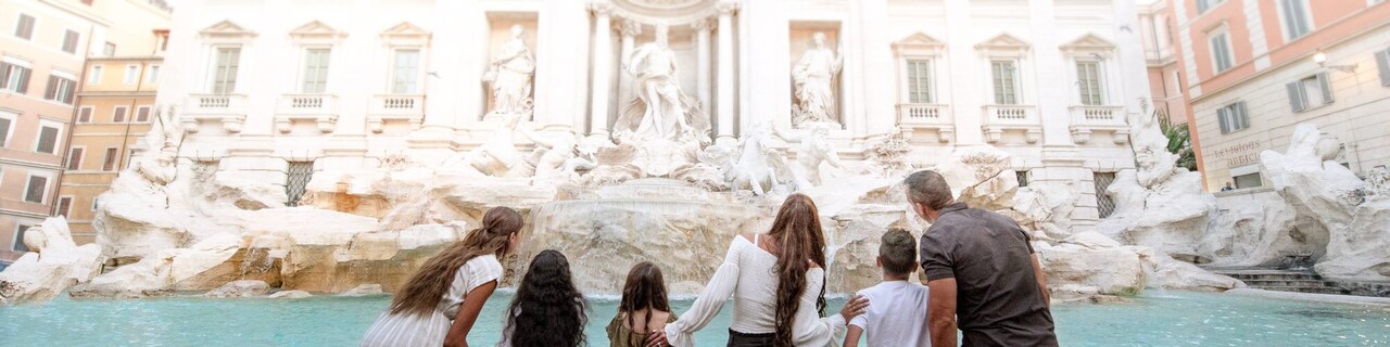 A family of six stands in front of the Trevi Fountain