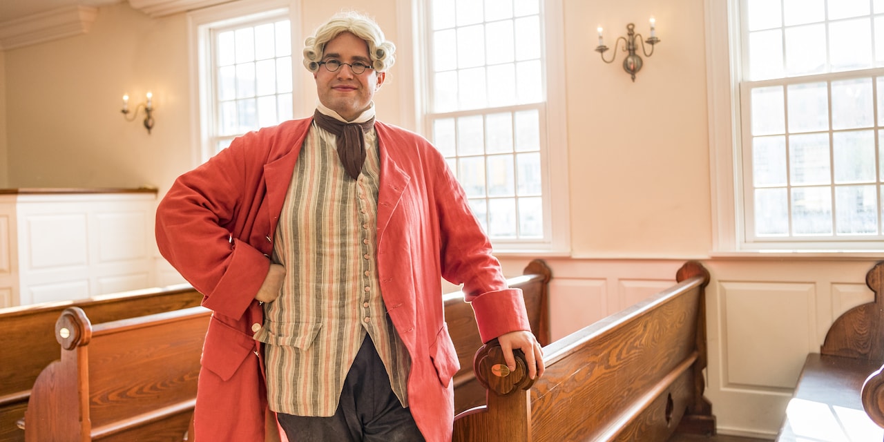 A historical reenactor dressed in colonial attire strikes a pose inside a church A historical reenactor dressed in colonial attire strikes a pose inside a church