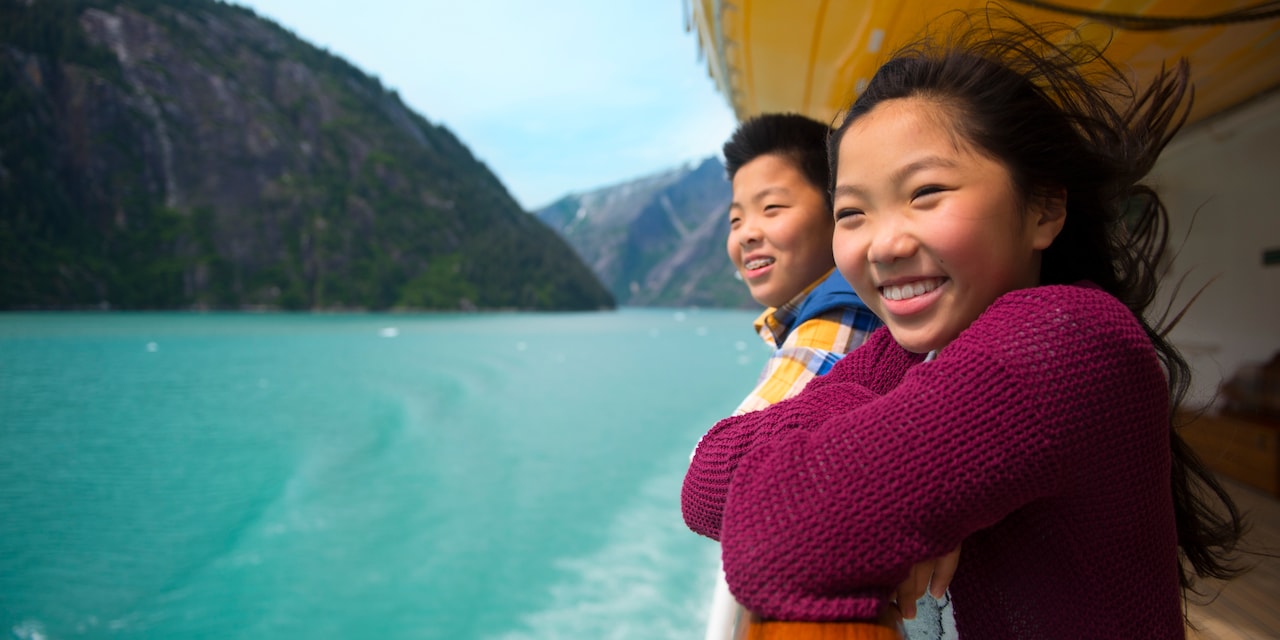 A young girl and boy are all smiles as they look at moutains and the ocean from a railing on a deck of the Disney Wonder cruise ship A young girl and boy are all smiles as they look at moutains and the ocean from a railing on a deck of the Disney Wonder cruise ship