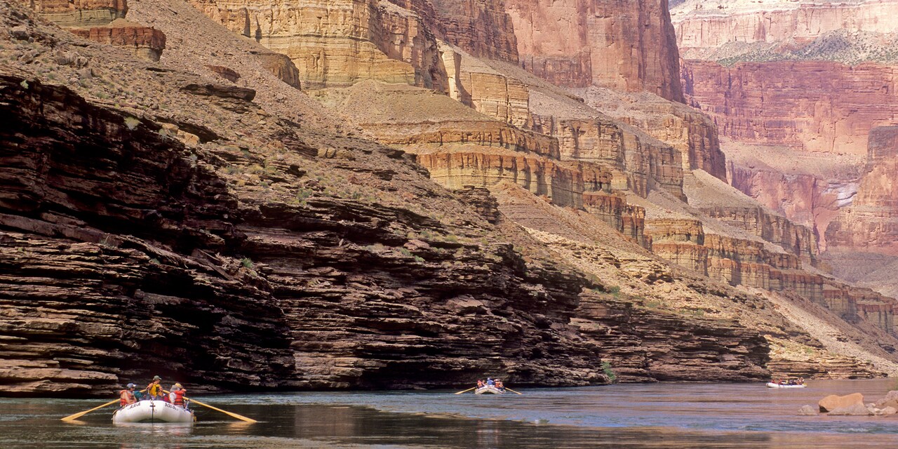 Adventurers raft down the Colorado River through a rock canyon Adventurers raft down the Colorado River through a rock canyon