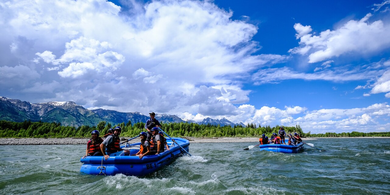 Two rafts filled with people, each paddled by a guide, ride through rapids on a river