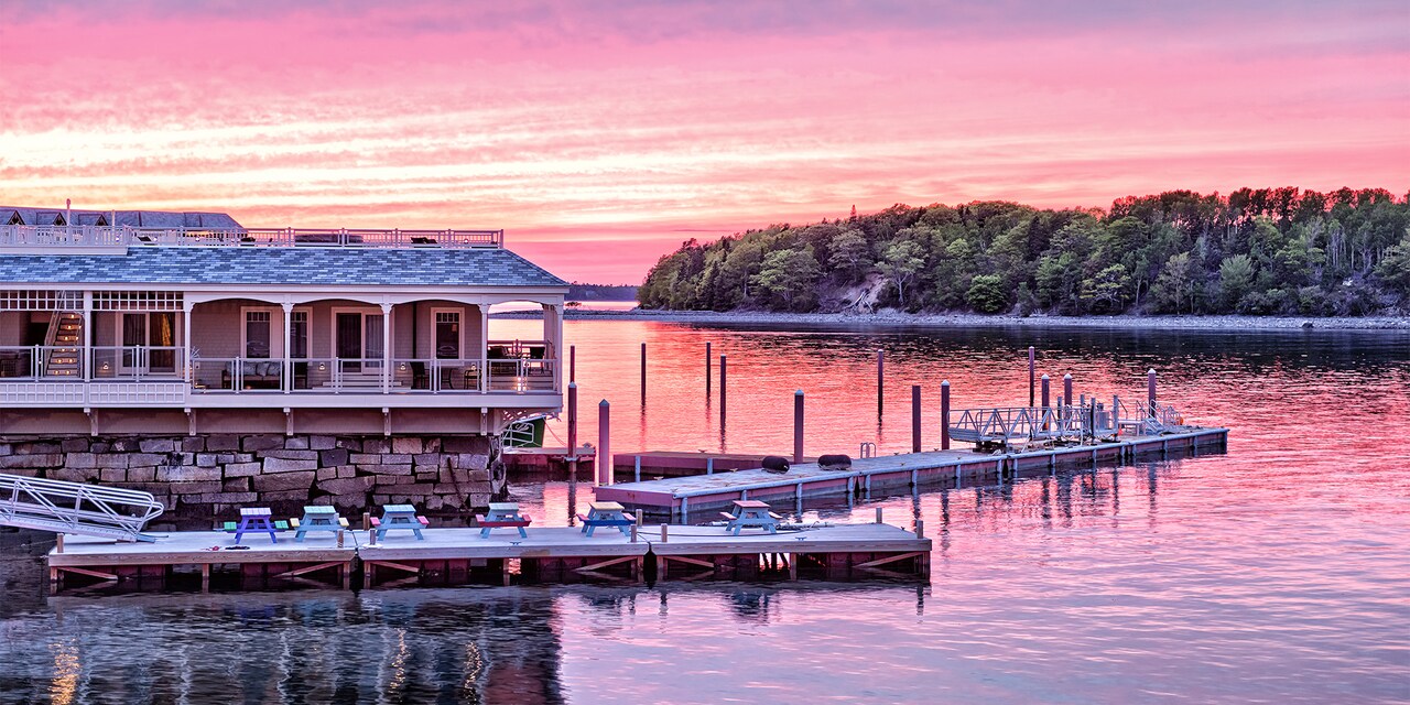 A house on the water in Bar Harbor, Main sits across the lake from a forest-lined river bank at sunset
