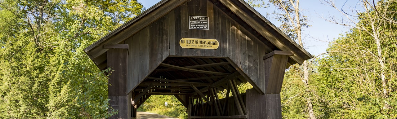 A road heading under a wooden covered bridge with a sign that reads ‘No Trucks or Buses Allowed’