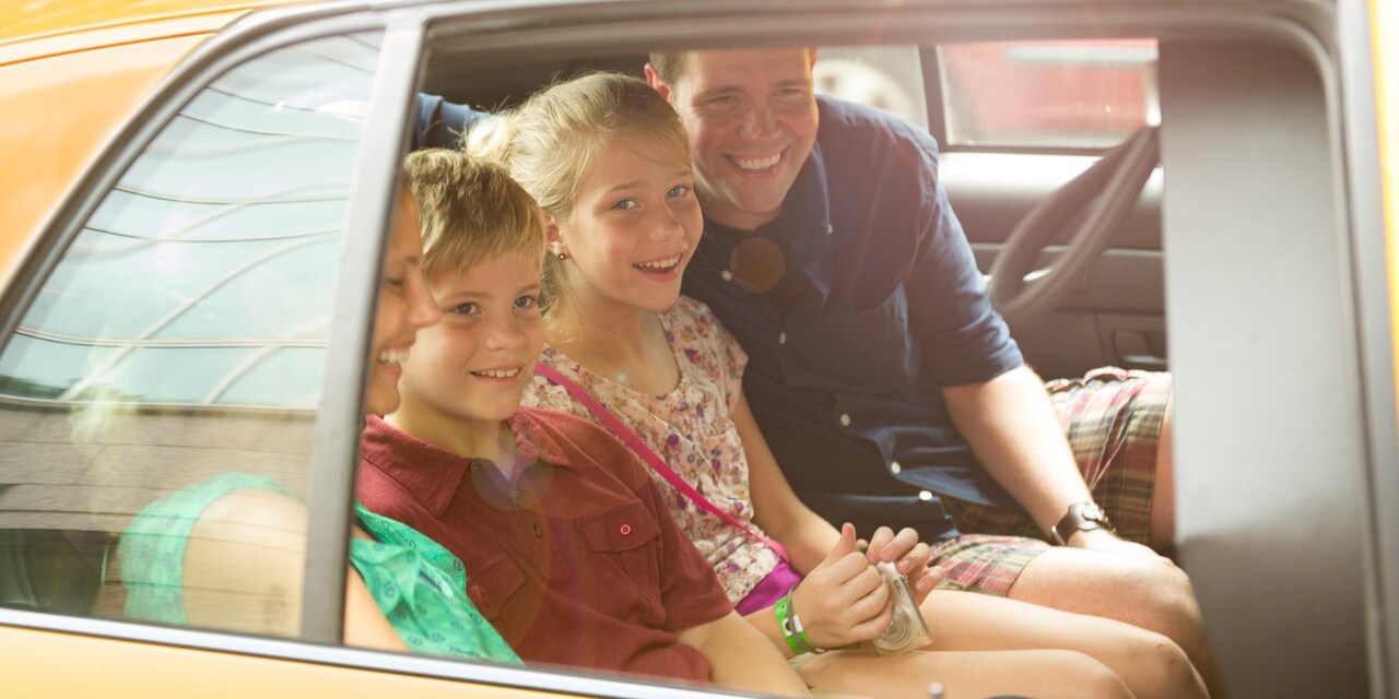 A smiling family of 4 rides in the back of a sedan A smiling family of 4 rides in the back of a sedan