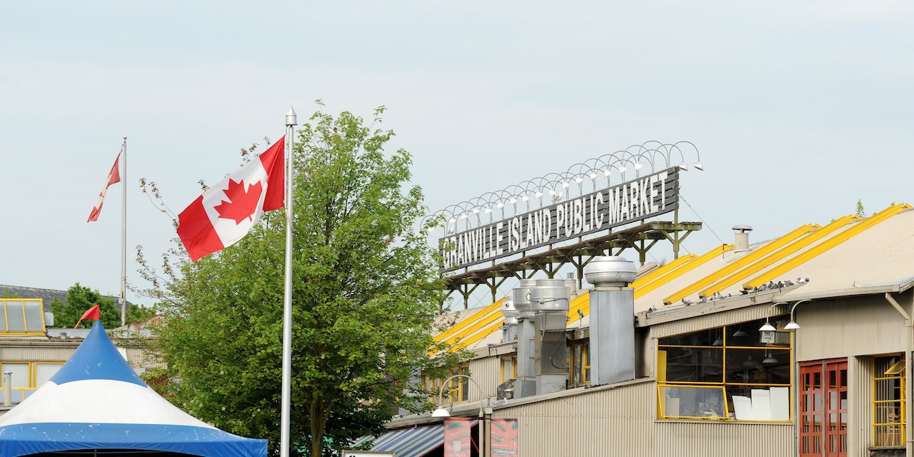 A Canadian flag waves in front of a rooftop sign that reads, “Granville Island Publilc Market” A Canadian flag waves in front of a rooftop sign that reads, “Granville Island Publilc Market”