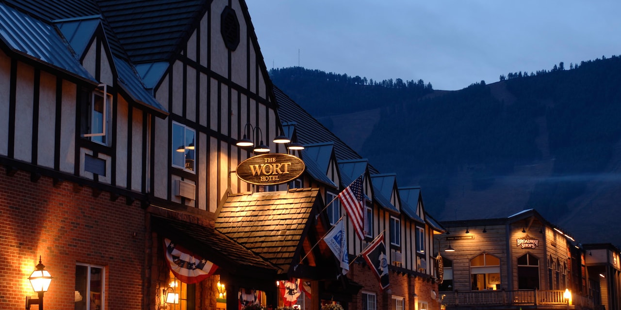 At night, a lit sign above the entrance to a building made of wood and brick reads 'The Wort Hotel'
At night, a lit sign above the entrance to a building made of wood and brick reads 'The Wort Hotel'
