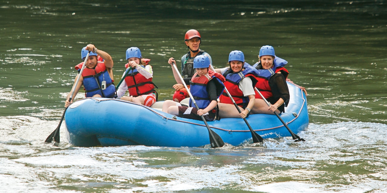6 people wearing athletic helmets paddle down a river in a raft 6 people wearing athletic helmets paddle down a river in a raft