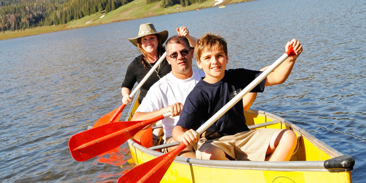 A boy and 2 adults paddle down a river in a rowboat A boy and 2 adults paddle down a river in a rowboat