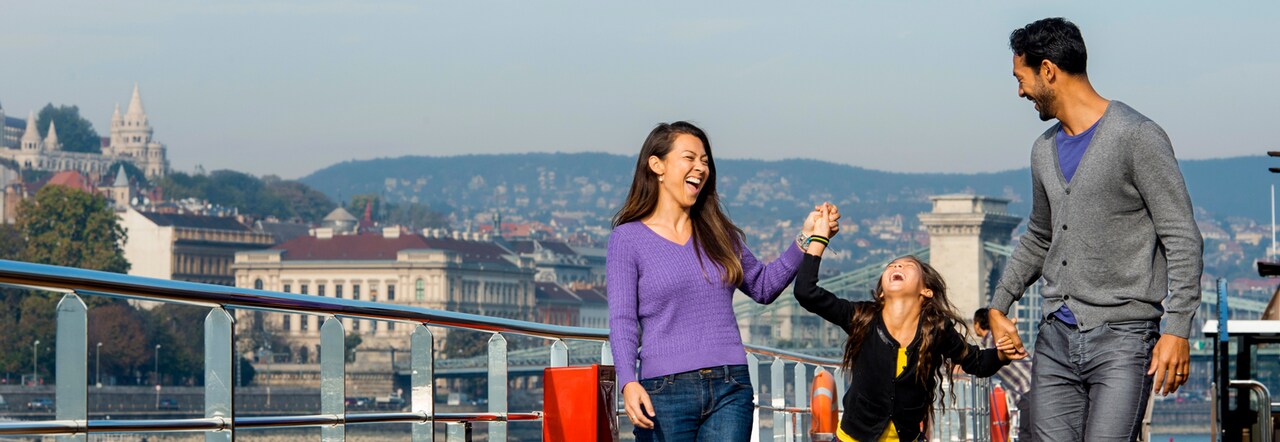 A young girl and her parents hold hands while walking on the deck of a river cruise ship sailing through Budapest, Hungary
