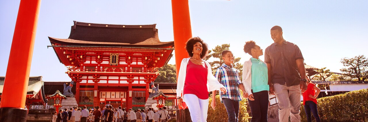 A family of 4 walks past a torii gate near the entrance to Fushimi Inari Shrine in Kyoto, Japan