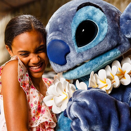 A girl smiles while giving Stitch a hug