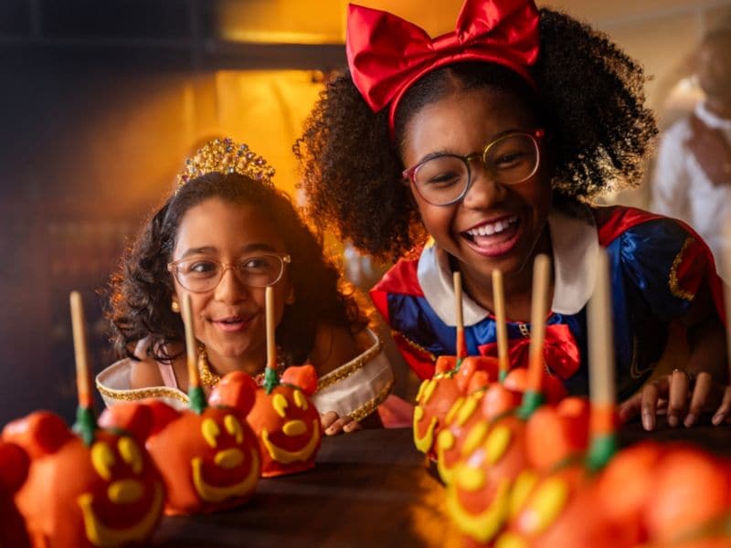 Two girls dressed as Snow White and Aurora looking at Halloween themed Mickey Mouse candy apples