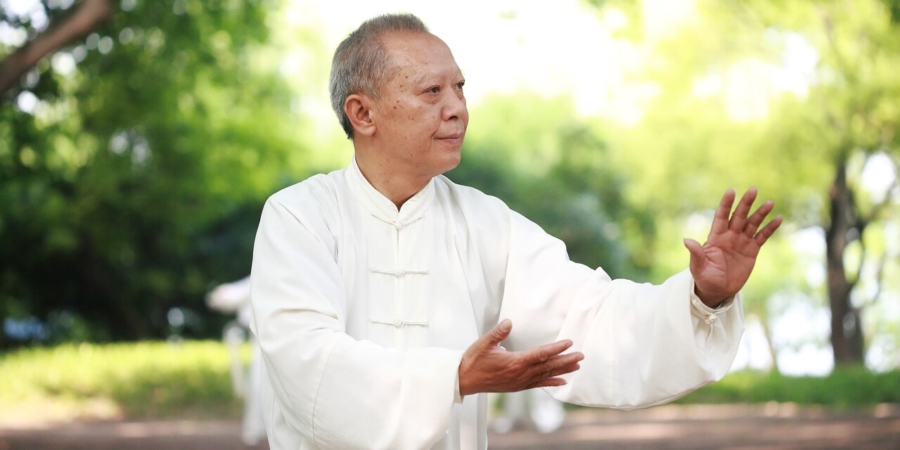 An older man practices Tai Chi in a park