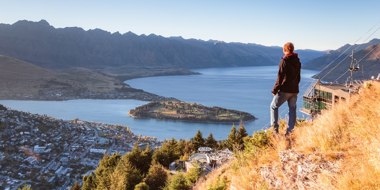 A man stands on a hill looking down on the city of Queenstown and Lake Wakatipu