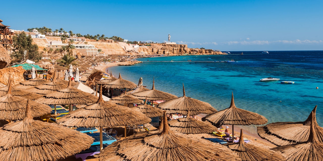 Rows of thatched umbrellas and chaise lounges line sand of the cliffside beach near the Red Sea