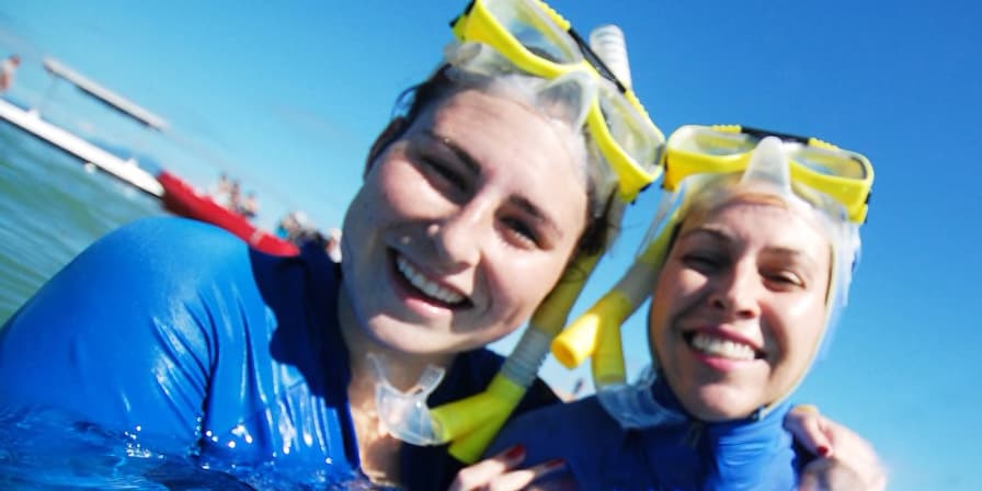 2 smiling teenage girls dressed in wet suits tread water and hold snorkel gear