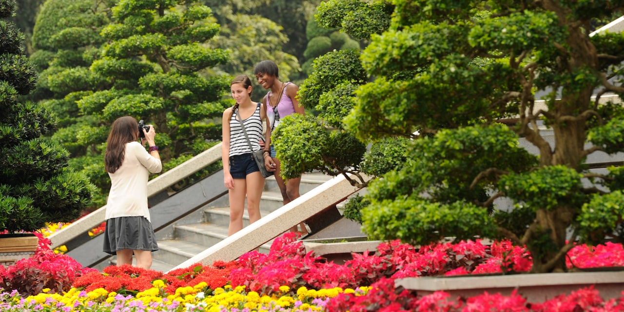 A woman takes a picture of her 2 friends standing on a stairway in a tropical garden
