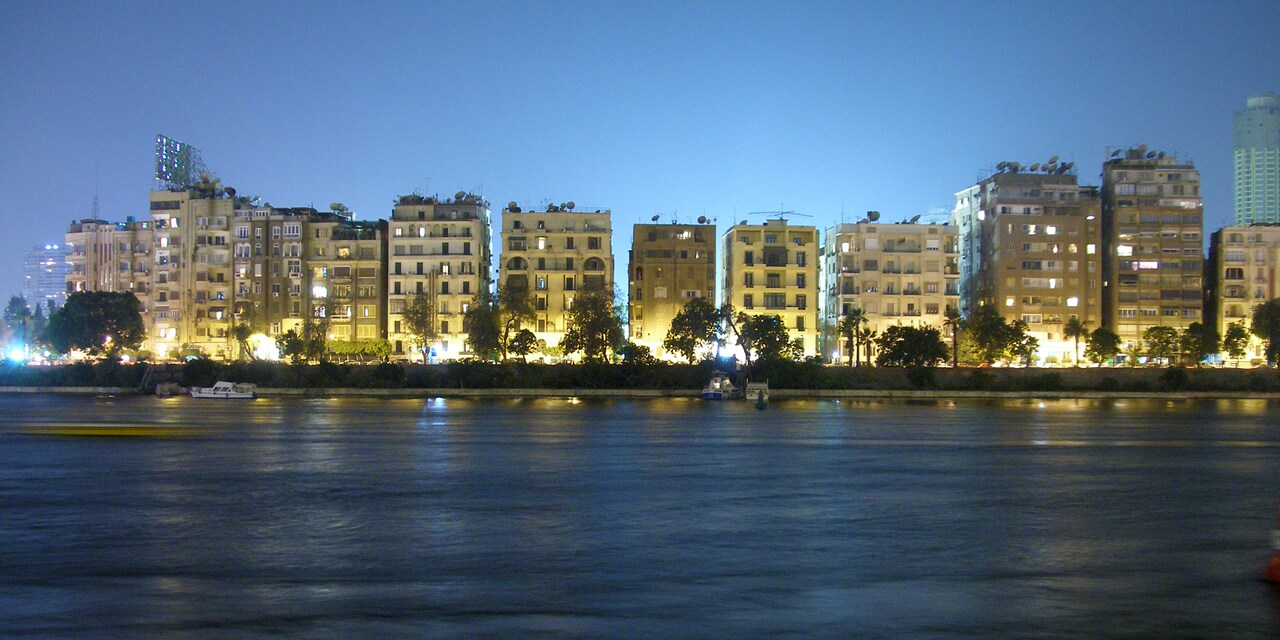 Lit up buildings of the Cairo, Egypt skyline along the Nile River at dusk