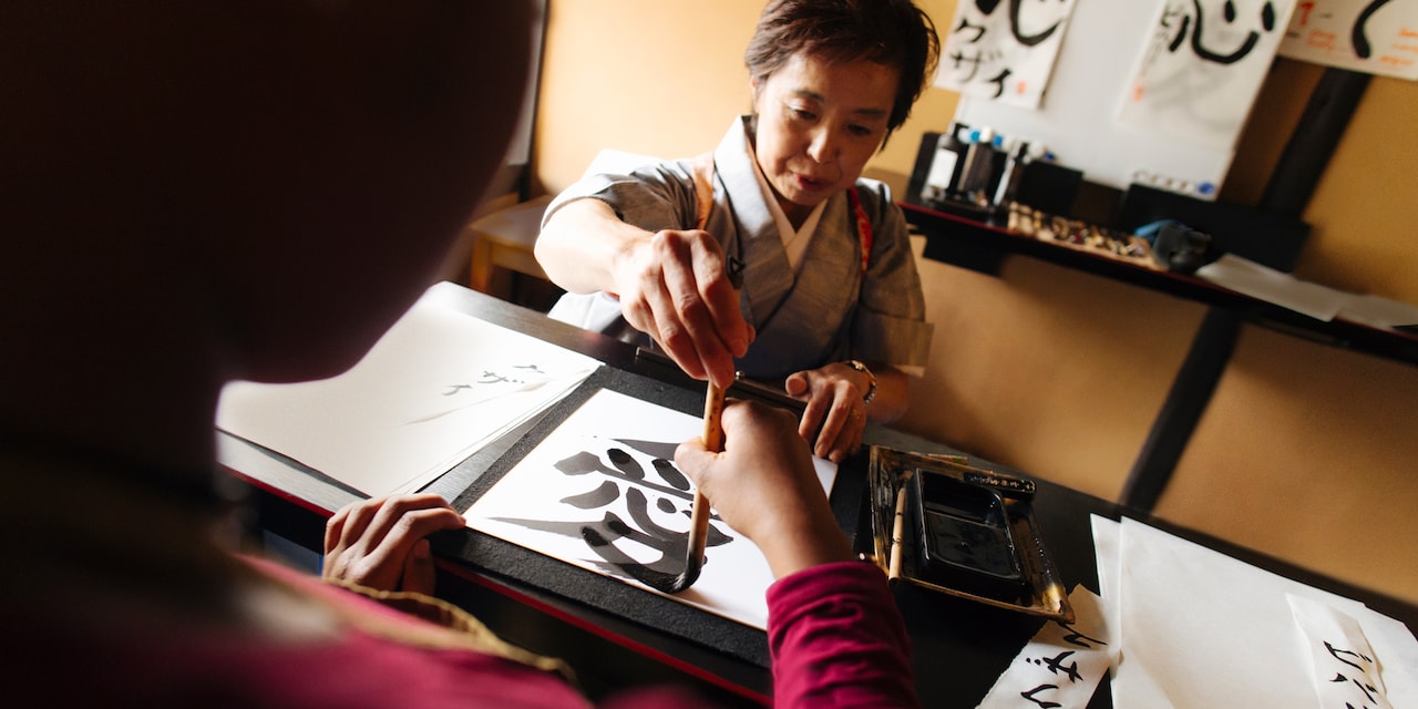 A Japanese woman helps guide the brush of a woman learning calligraphy 
