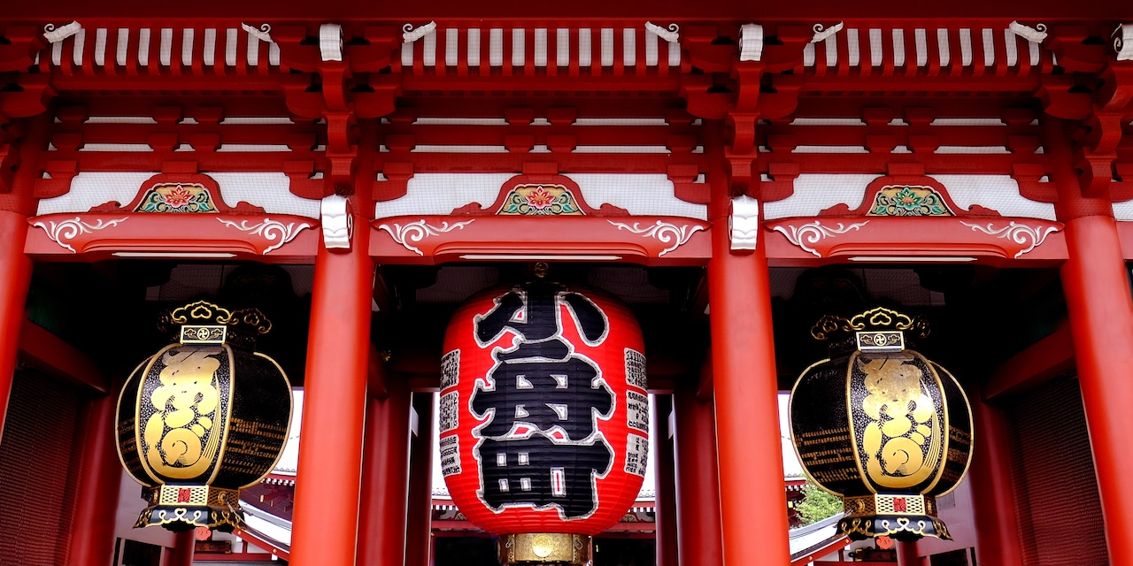 A large, red lantern hangs between to smaller lanterns outside a temple