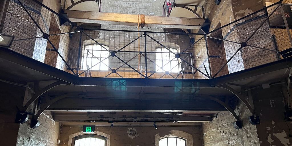 A 2nd floor walkway with metal railing and windows inside the stone Old Melbourne Gaol