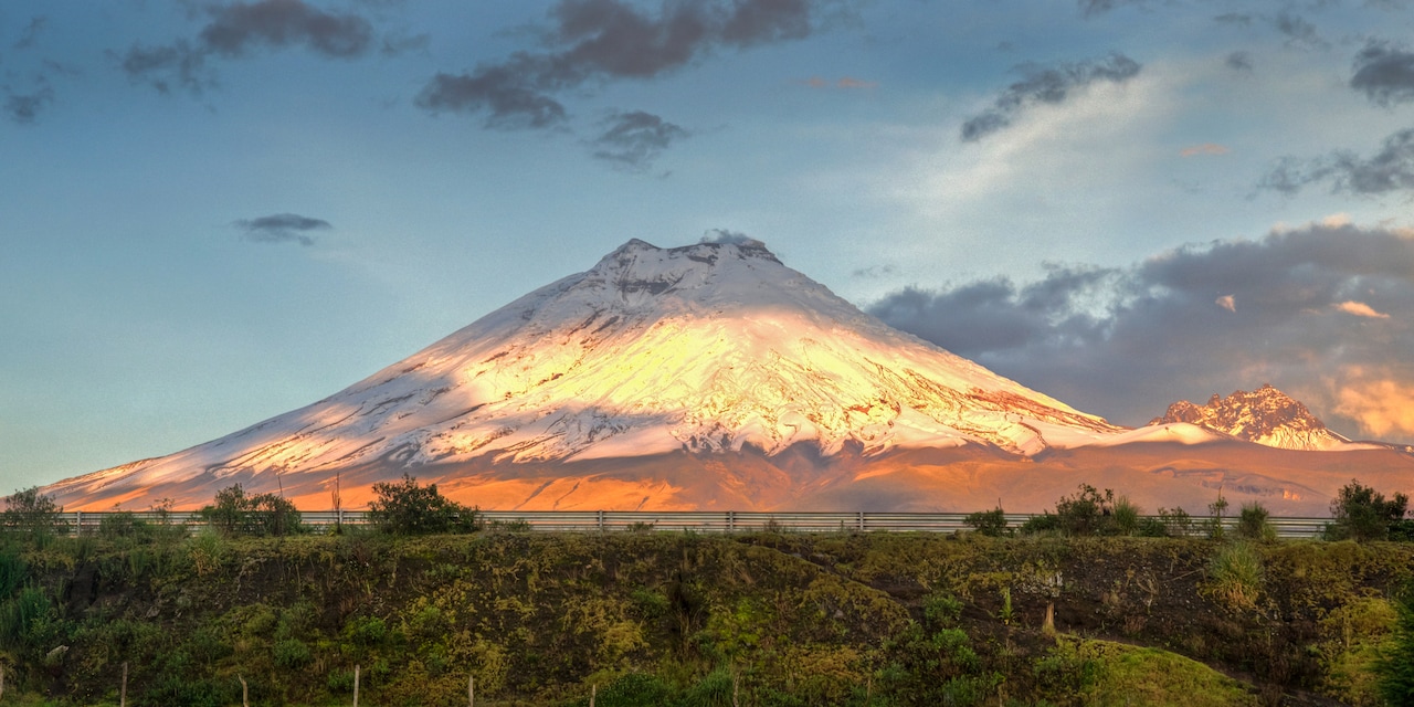 Cotopaxi volcano looms high above a lush, tree filled area near Quito, Ecuador