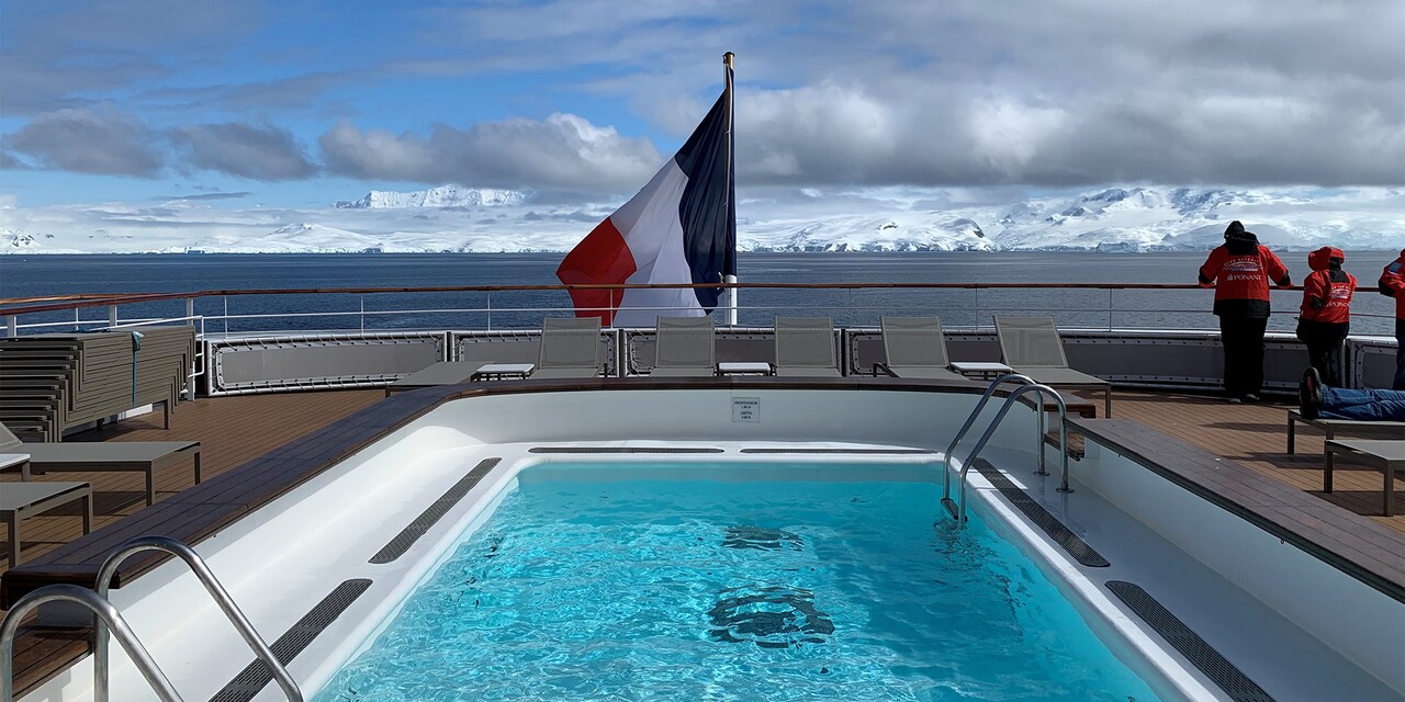 Top deck pool looking out to the French flag posted at the stern of the boat and the snowcapped mountains of Antarctica in the distance