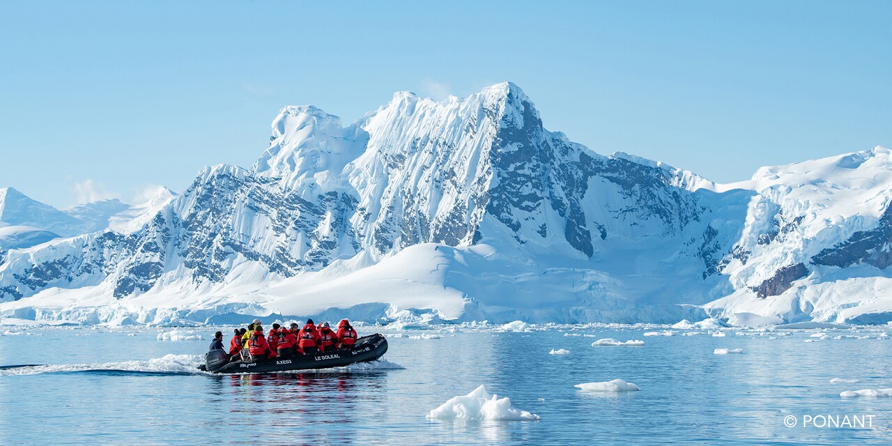 Group of parka clad Adventurers in a Zodiac boat navigating a strait to reach the snowy Antarctica shore
