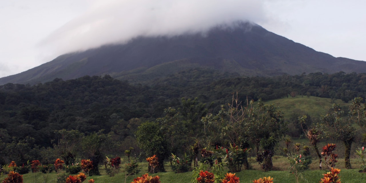 A lush landscape of grass and trees leads up to the cloud-covered Arenal Volcano in Arenal, Costa Rica