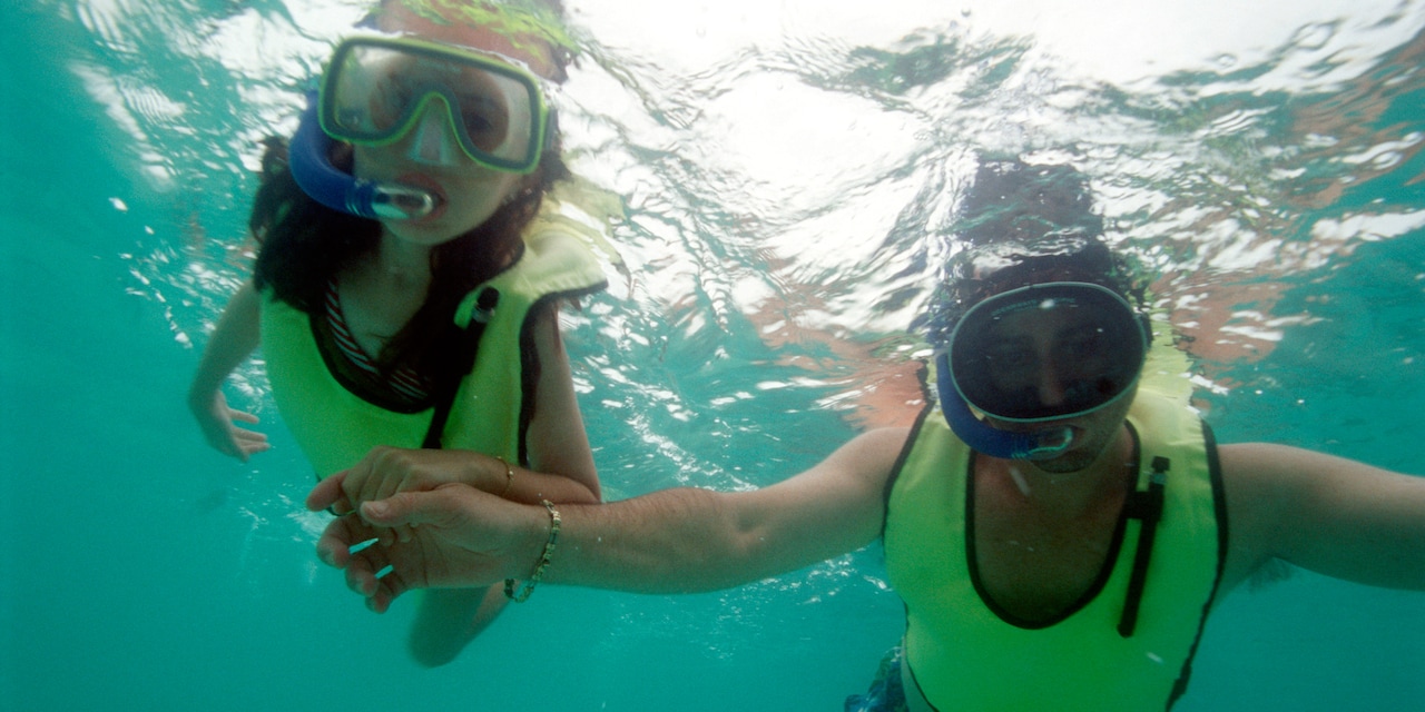 A couple hold hands while snorkeling underwater wearing snorkeling masks and vests