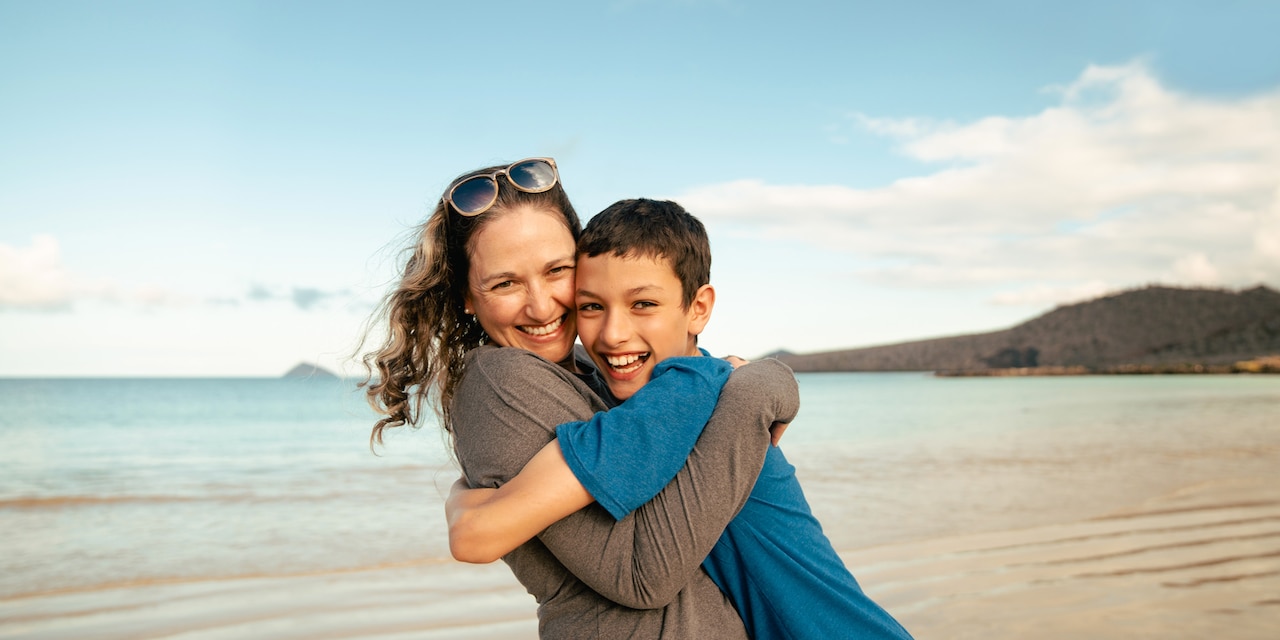 A woman hugs a young boy near the sea