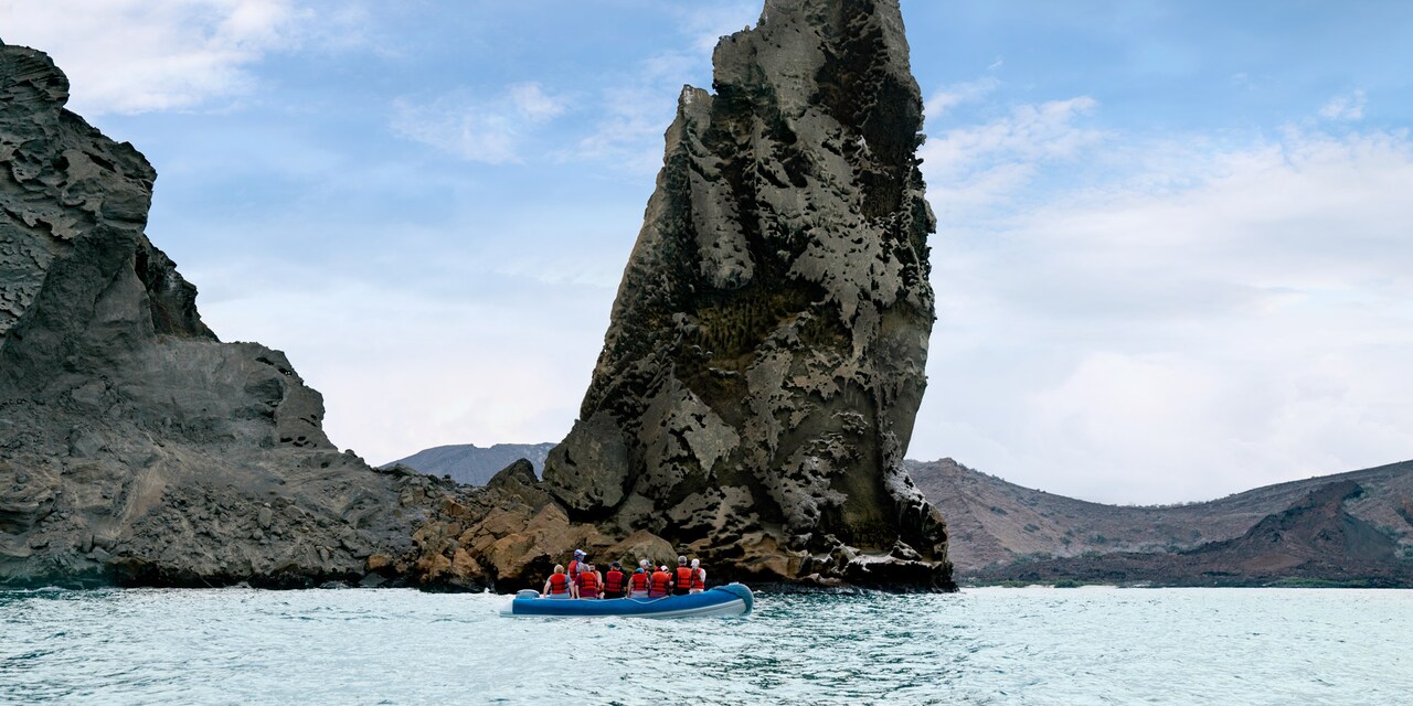 A group of people in a panga boat ride on the water near large rocks