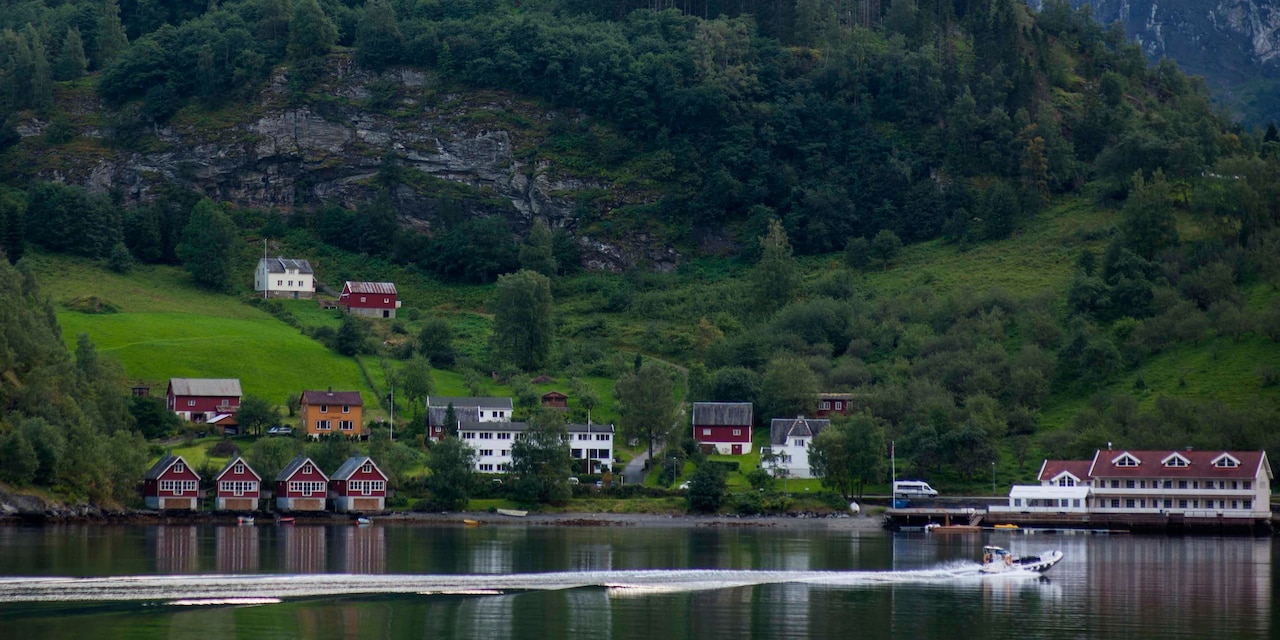 A motorboat passes a lakeside village with houses extending up the mountainside
