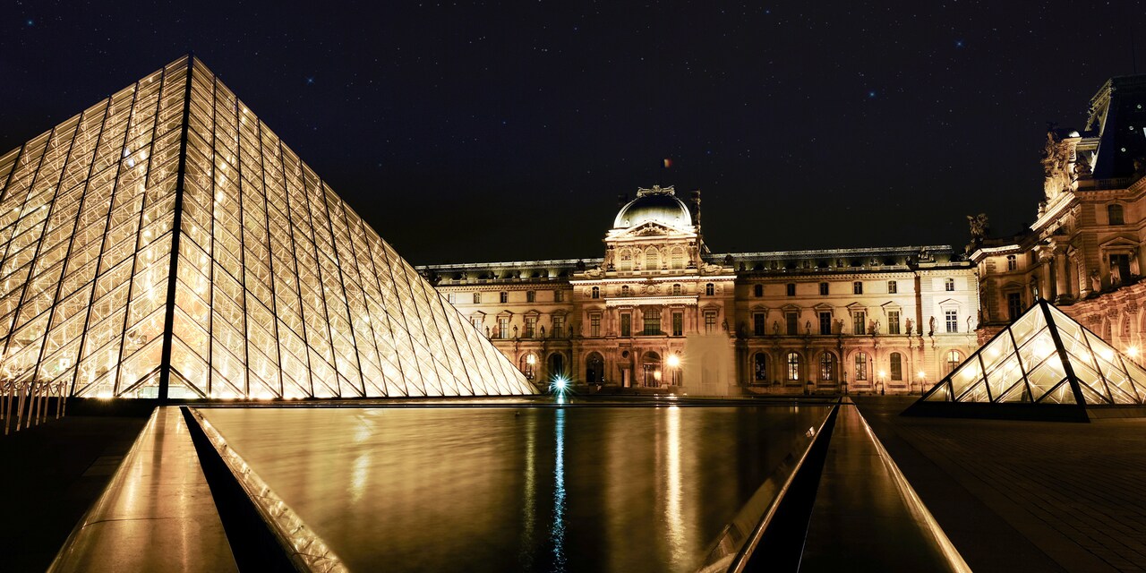 The glass pyramids and the main building of the Louvre Museum in Paris, France lit up at night