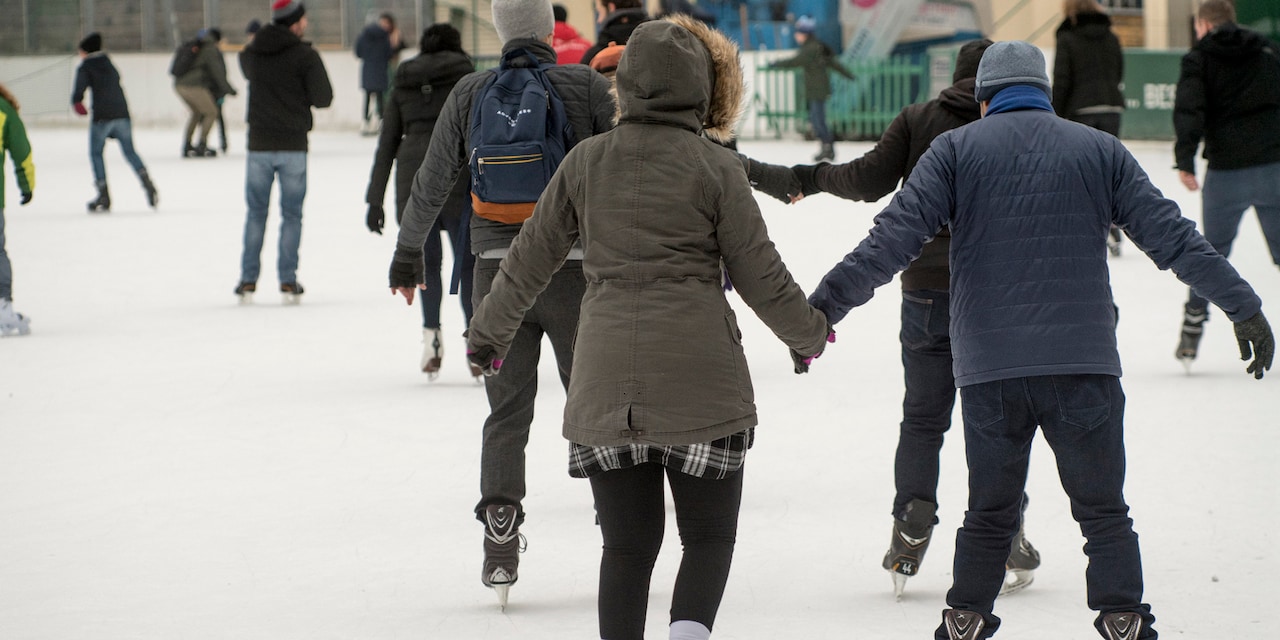 People dressed in warm jackets ice skate on an outdoor ice rink