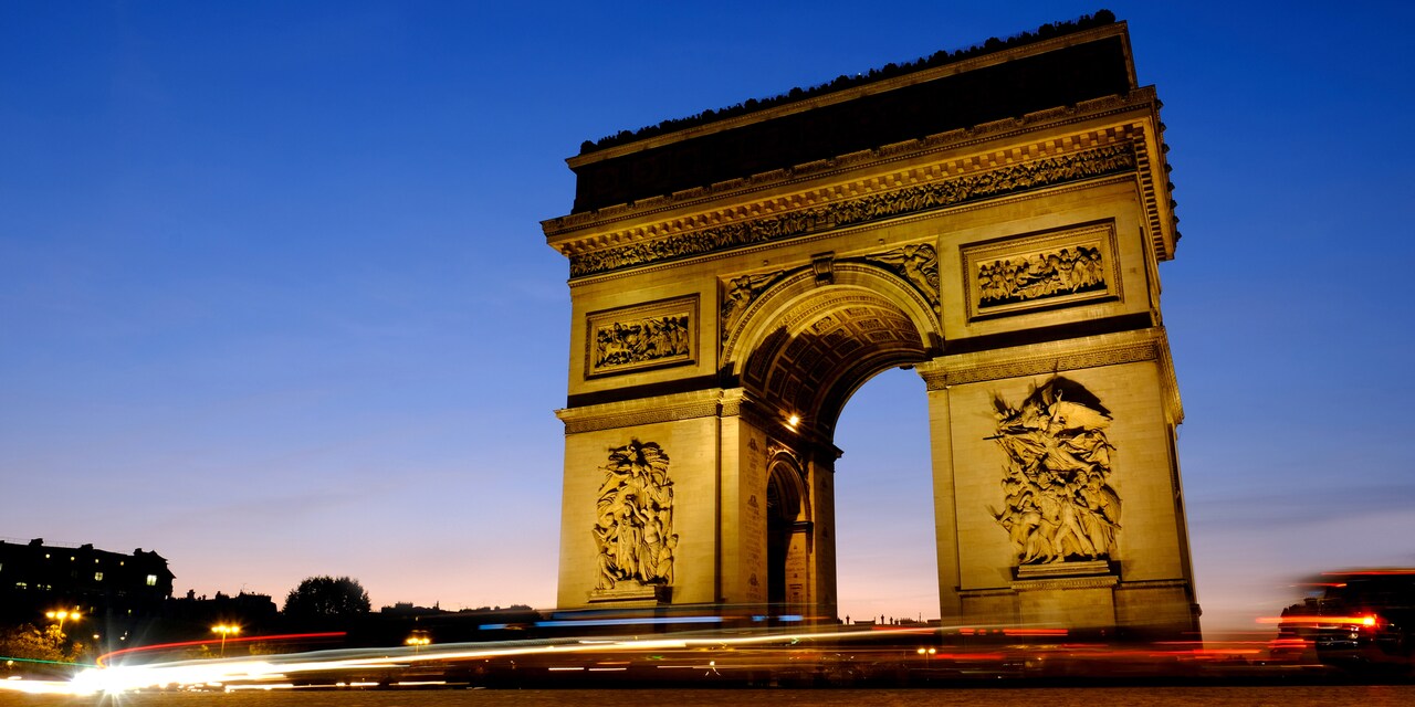 The Arc de Triomphe lit up at night at dusk in Paris, France