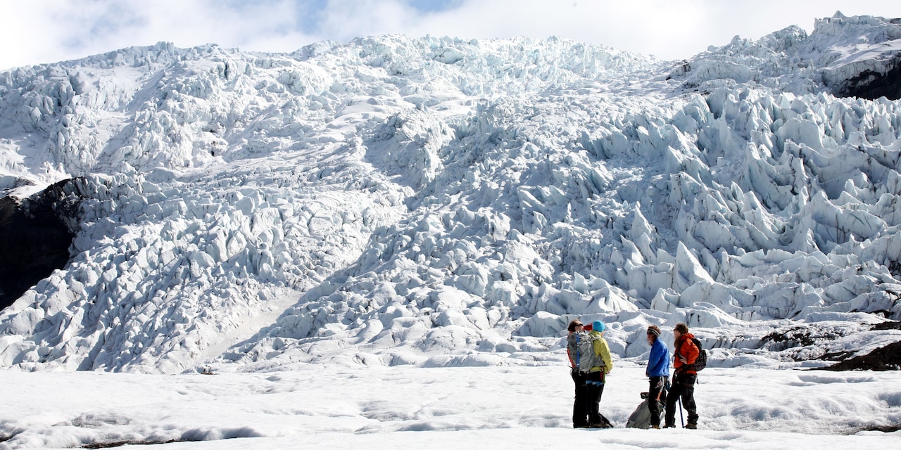 A group of hikers gather at the base of a glacier