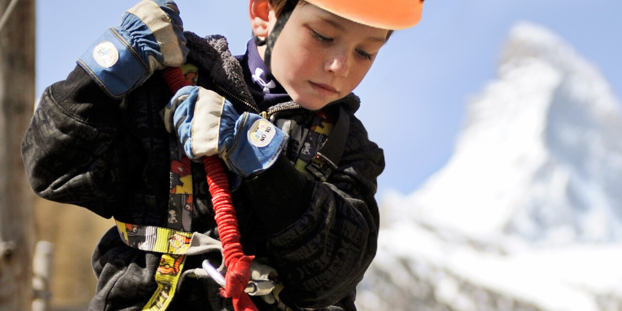 A boy wearing an athletic helmet grasps a rope with his gloved hands