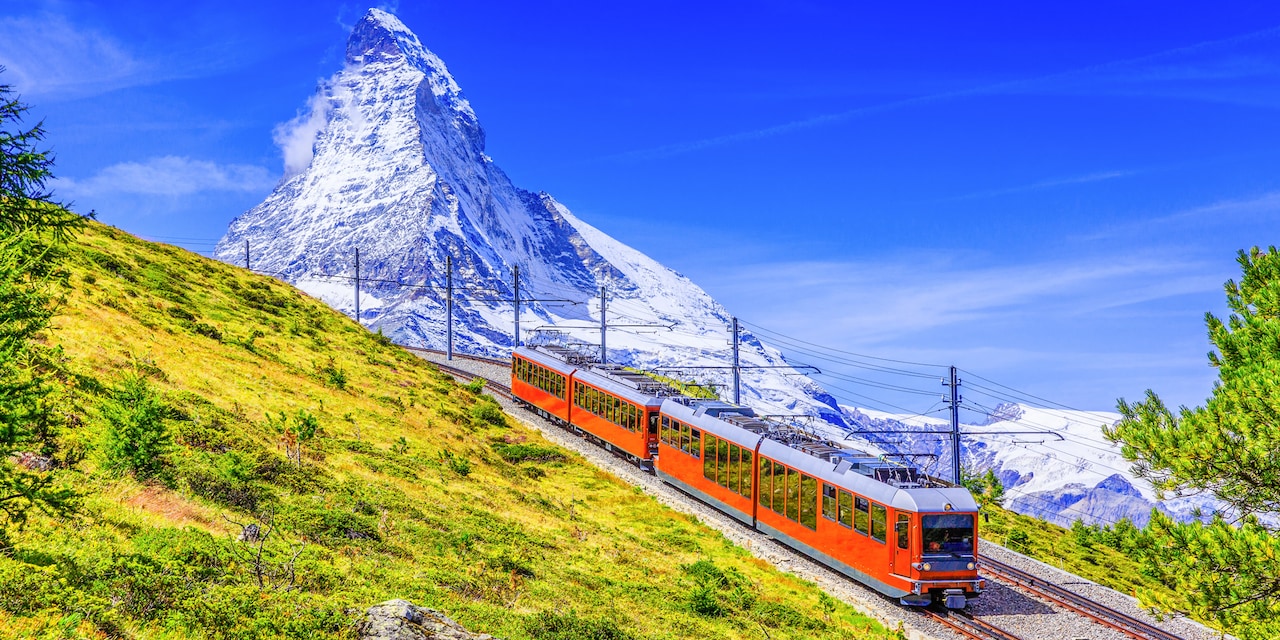 A train heading down a hill away from a snowy mountain