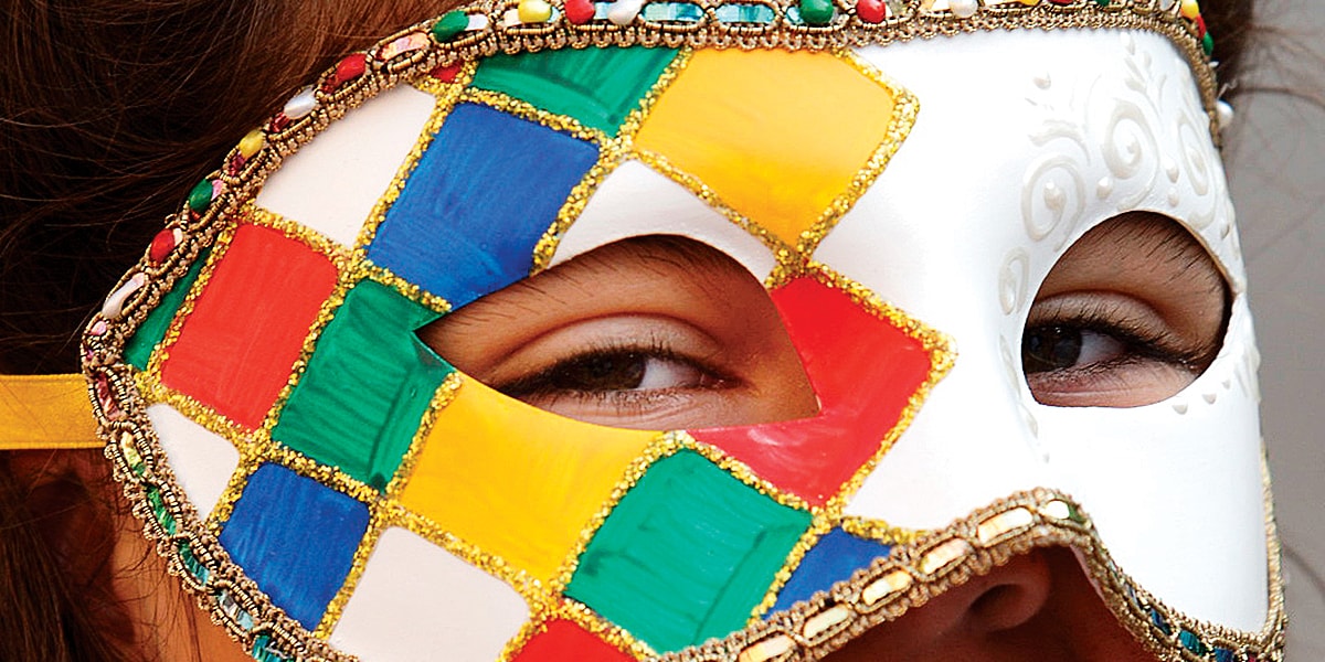 Person wearing a mask decorated with a multicolor ribbon border and diamonds on one side
